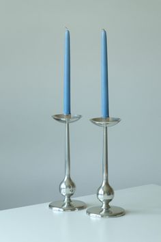 two silver candlesticks with one blue candle in the middle on a white table