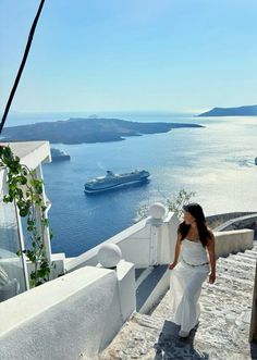 a woman in white is walking down the stairs towards the water and cruise ship on the other side