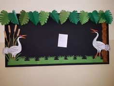 two cranes are standing in front of a black board with palm trees and grass on it