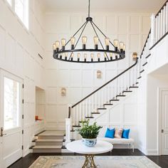 a living room filled with furniture and a chandelier hanging from the ceiling next to a stair case