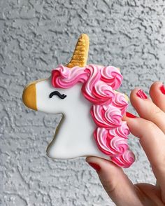 a hand holding a cookie shaped like a unicorn with pink frosting and a gold horn