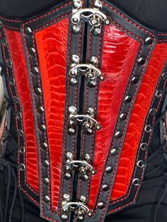 Hand made leather under bust corset in Red/Black or Turquoise/Black Colors . Corset panels feather Ostrich Leg Leather inlays for an Exotic look. This corset is designed to fit all sizes from 0 to 24. It has removable side panels to fit the small end of the size spectrum. There are five lacings to adjust to all sizes when side panels are used. 3 Lacings when the side panels are not used**. The front opens and closes easily and conveniently with five swing clasps once the corset is adjusted to your size. All Lacing is fully grommeted . All hardware is silver finish  (Swing Clasps, rivets, lacing grommets) As this is a full cowhide leather corset, there are no bonings needed. Inside is finished full grain leather and hand dyed to black The front panels are made from 3 ounce  with Ostrich Leg Steampunk Leather Corset For Cosplay, Gothic Leather Corset For Cosplay, Gothic Leather Corset For Party, Gothic Leather Overbust Corset, Fitted Leather Corset For Cosplay, Red Gothic Overbust Corset, Red Underbust Corset For Cosplay, Steampunk Red Overbust Corset, Red Halloween Corset With Corset Back