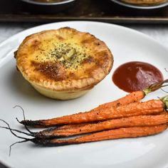 some carrots are on a plate next to a pot pie and sauce for dipping