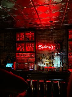 a dimly lit bar with red neon lights and bottles on the shelves, along with stools