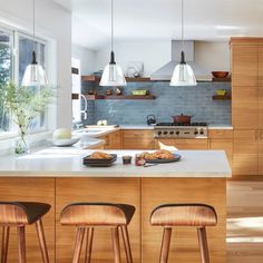 a kitchen with wooden cabinets and stools in front of the counter top, along with three lights hanging from the ceiling