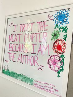 a sign that is on the wall in front of a whiteboard with writing and flowers