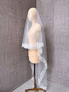 a mannequin wearing a white veil on top of a wooden stand in front of a gray wall