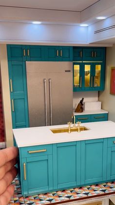 a hand is holding a toy kitchen with blue cabinets