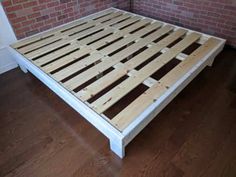 a bed frame made out of wood sitting on top of a hard wood floor next to a brick wall