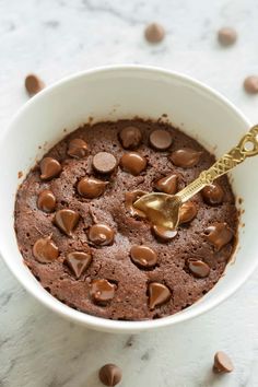 a white bowl filled with chocolate pudding and topped with a gold spoon, on top of a marble surface