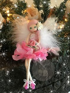 a pink and white doll sitting on top of a black table next to a christmas tree