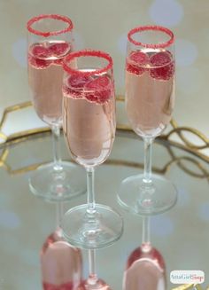 three wine glasses filled with pink liquid and garnished with red glitters on the rim