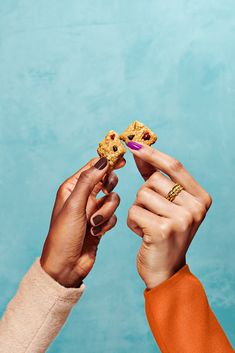 two people are holding cookies in their hands against a blue background and one is reaching for the cookie