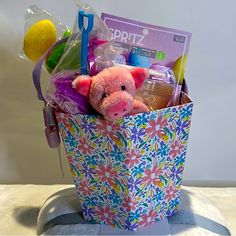 a pink stuffed animal sitting inside of a colorful gift bag on top of a table