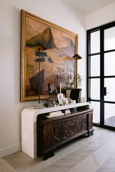 a living room with a painting on the wall next to a table and lamp in front of it