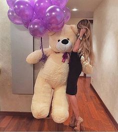 a woman standing next to a giant teddy bear with balloons on it's head