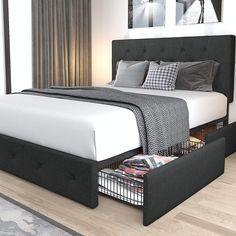 a bed with two drawers underneath it in a white and black bedroom, along with pictures on the wall