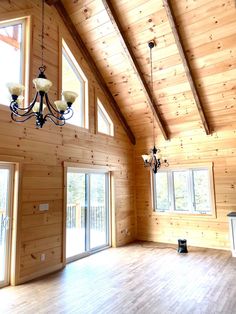 an empty living room with wood paneling and chandelier hanging from the ceiling