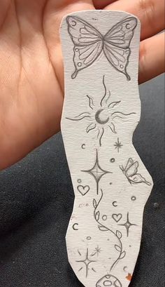 a hand holding a piece of paper with designs on it and a butterfly painted on the back