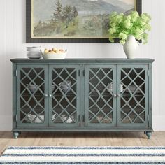 a blue sideboard with glass doors and vases on it in front of a painting