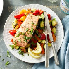 a white plate topped with salmon and veggies next to a bowl of sauce