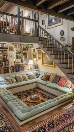 a living room filled with lots of furniture and bookshelves next to a stair case