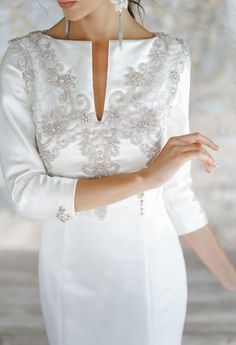 a woman wearing a white dress and pearls in her hair, standing with her hands on her hip