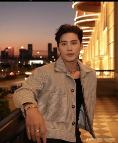 a young man standing on top of a balcony next to a tall building at night