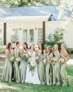 a group of women standing next to each other in front of a white house and holding bouquets