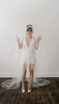 a woman in a white dress and veil standing on a wooden floor with her hands up