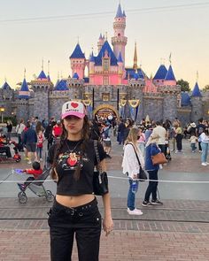 a woman standing in front of a castle wearing a baseball cap and black pants with her hands on her hips