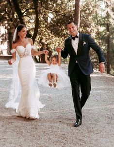 a bride and groom are holding hands as they walk through the park with their daughter