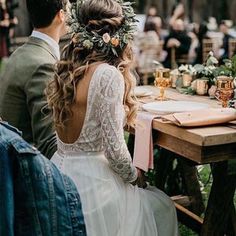 the back of a bride's dress sitting at a table with flowers in her hair