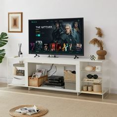 a flat screen tv sitting on top of a white entertainment center next to a potted plant