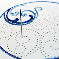 a needle is in the middle of a piece of paper with blue designs on it