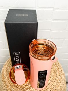 a pink cup sitting on top of a straw hat next to a black box with a tag