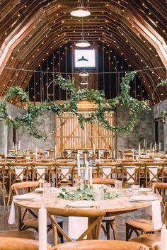 the inside of a barn with tables and chairs set up for a wedding reception, surrounded by greenery