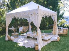 a white tent set up in the middle of a yard with pillows and chairs around it