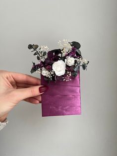 a hand holding a purple paper bag with flowers in it on a gray background,