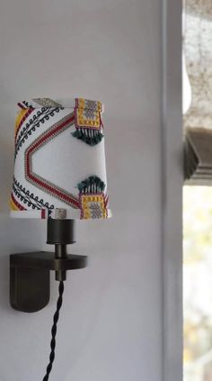 a lamp that is on the wall next to a light fixture with a fabric shade