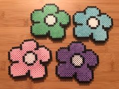 four different colored flowers made out of perler beads on a wooden surface with one flower in the middle