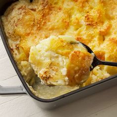 a casserole dish with potatoes and cheese in it, being lifted by a spoon