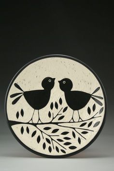 two black birds sitting on top of a tree branch in front of a white circle