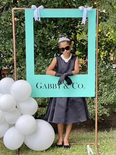 a woman standing in front of a blue sign with balloons and a balloon arch behind her