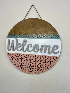 a welcome sign hanging from the side of a white wall with blue and pink accents