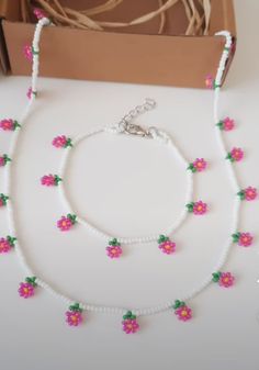 two necklaces with pink flowers on them sitting next to a box and some string