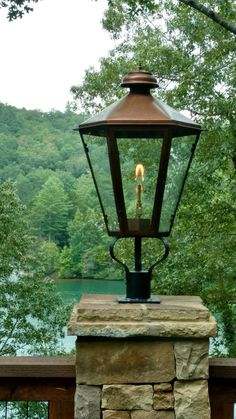 a lamp on top of a stone pillar next to a body of water with trees in the background