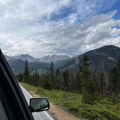 a car driving down a road with mountains in the back ground and trees on both sides