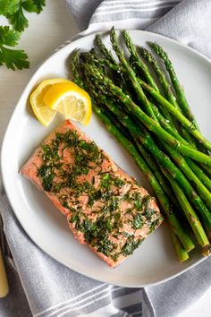 salmon and asparagus on a white plate with lemon wedges next to it