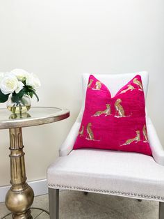 a white chair with a pink pillow on it next to a small table and flowers